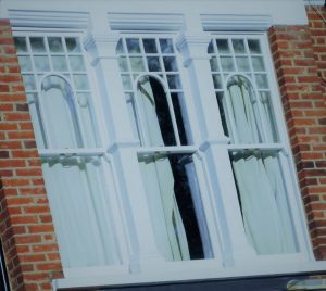 A zoomed in photo of a set of three white sash windows installed into a brick built house.