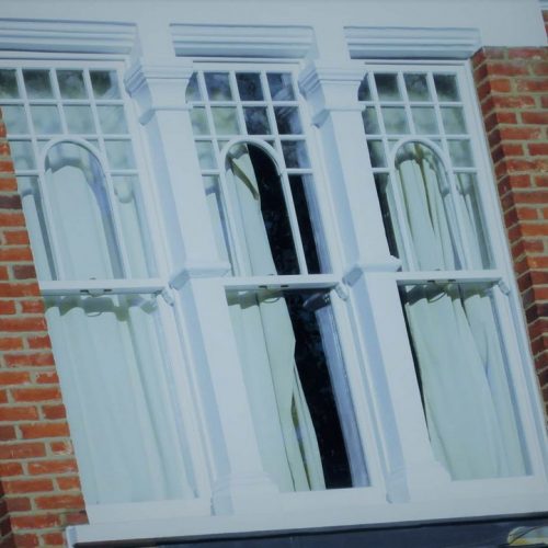 A zoomed in photo of a set of three white sash windows installed into a brick built house.